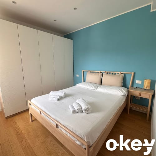 Camera moderna presso Okey Homes Bari con letto in legno, parete azzurra, armadio bianco e pavimentazione in legno