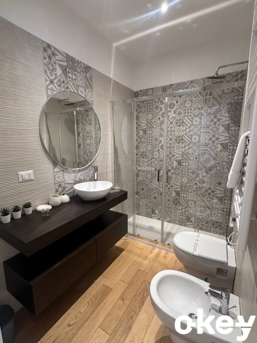 Bagno moderno di Casetta Lilla Stay Bari con doccia in piastrelle decorate, specchio rotondo, lavabo a bacinella e pavimentazione in legno