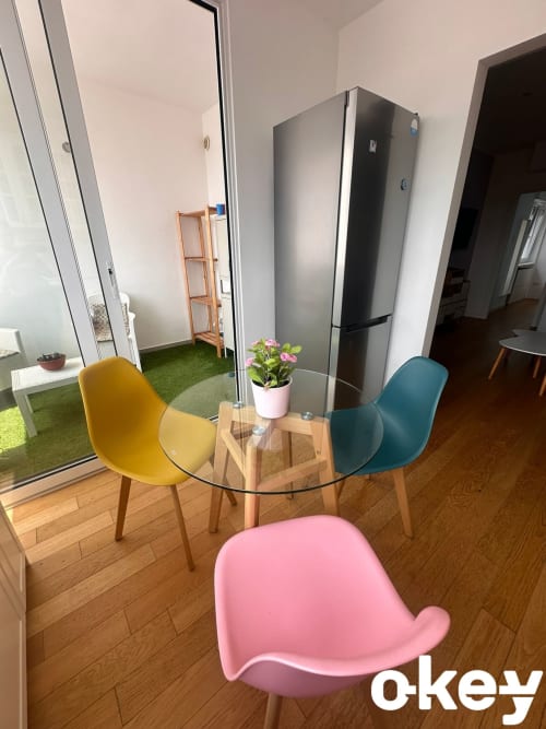 Elegante sala da pranzo moderna nell'appartamento di Bari con tavolo in vetro, sedie gialle, turchesi e rosa, pavimento in legno e cucina