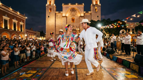Pareja bailando con traje tradicional colorido en festival de plaza de Mérida con catedral y multitud nocturna