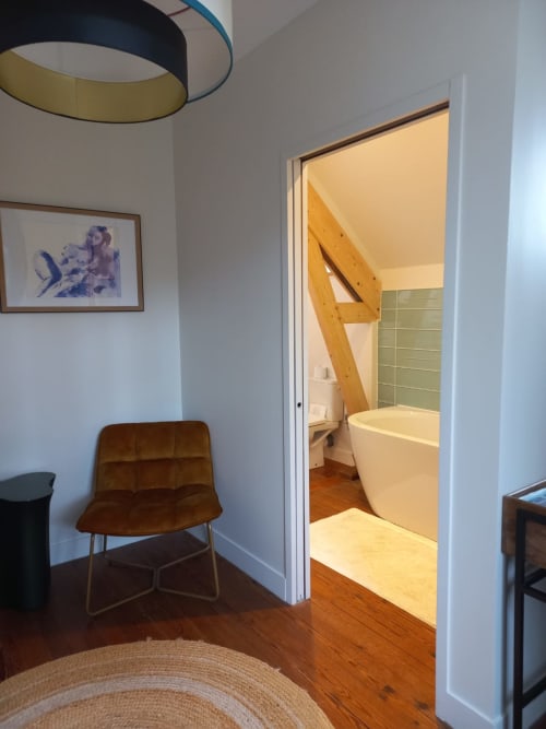 Suite Deluxe bedroom at Villa Eliane in Étretat with brown chair and open doorway to bathroom with bathtub and wooden stairs