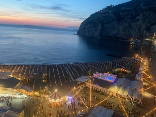 Sorrento Sea View beach venue at twilight with illuminated seating, stage, and dramatic coastal cliffs in Meta, Italy