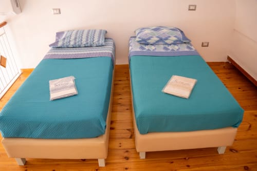 Two twin beds with turquoise covers in Sorrento Sea View apartment, wooden floor, welcome packages on beds