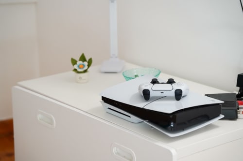 Modern gaming setup at Sorrento Sea View hotel with PlayStation 5, white controller, and decorative plant on desk