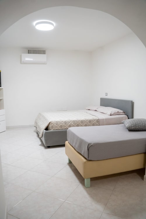 Minimalist bedroom at Sorrento Sea View with two beds, white ceiling, recessed lighting, and air conditioning unit