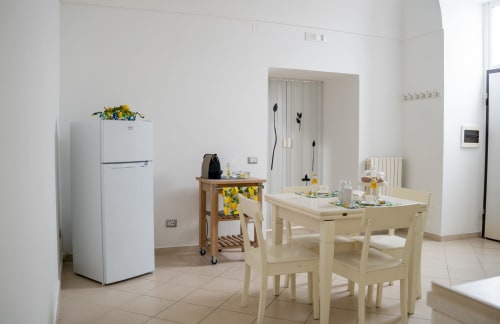 Light-filled apartment kitchenette and dining area at Sorrento Sea View with white appliances, wooden table, and cheerful