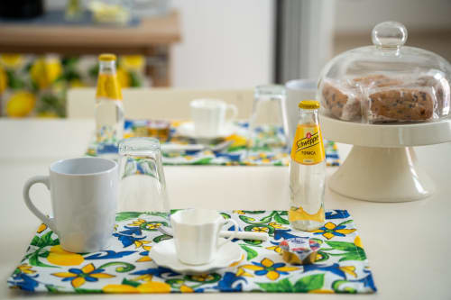 Bright kitchen setup at Sorrento Sea View with coffee mug, Schweppes bottle, and pastries in glass dome on floral placemat