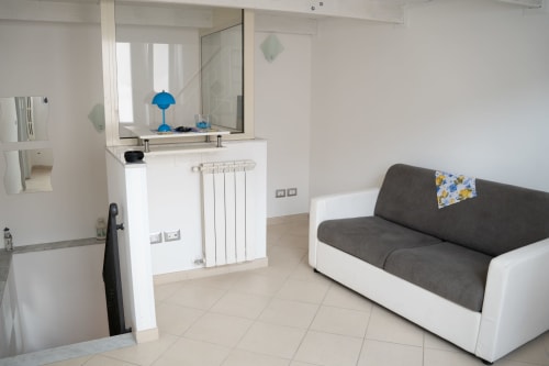 Modern studio apartment at Sorrento Sea View with gray sofa, kitchenette with mirror, radiator, and beige tile flooring in