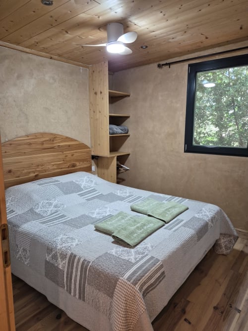 Gemütliches Schlafzimmer im Cottage L'andaréenne des Domaine en Terre Happy mit Holzbett, grünen Handtüchern und Gartenfenster