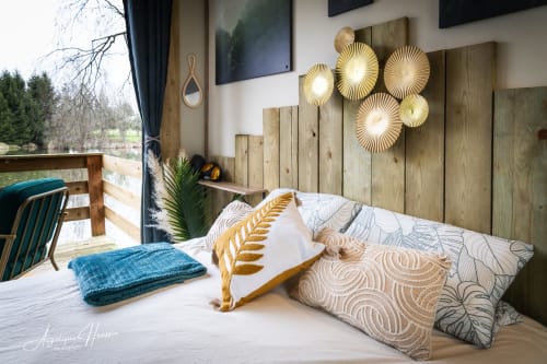 Chambre cosy à Les Rives du bel air avec accents en bois, éclairage doré, coussins à motifs et vue panoramique sur la forêt
