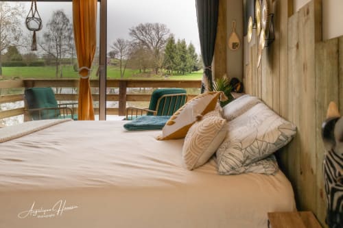 Chambre cosy dans une cabane perchée aux Rives du bel air, offrant une vue panoramique sur les prés verdoyants et les arbres à travers de grandes fenêtres