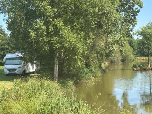 Camping-car blanc garé au bord d'une rivière bordée d'arbres à Les Rives du bel air, camping en zone rurale française