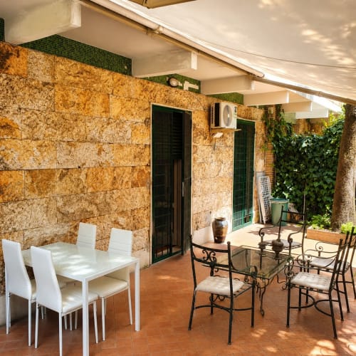 Garden-view terrace apartment in Rome with dining area, stone walls, and wrought iron seating