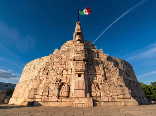Bandera mexicana en la cima de una escultura de pirámide Maya ornamentada en Mérida con cielo azul despejado