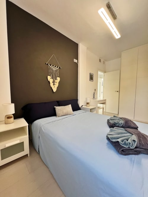 Dormitorio de lujo moderno en apartamento de Fuengirola con pared de acento oscuro, decoración de macramé y mobiliario contemporáneo