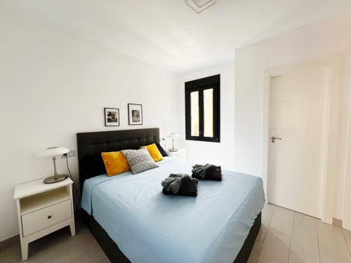 Dormitorio de apartamento de lujo moderno en Fuengirola con cabecero negro, ropa de cama azul, detalles amarillos y diseño contemporáneo