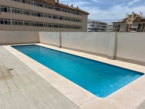 Piscina en la azotea del apartamento de lujo en Fuengirola con vistas a la ciudad y zona de descanso blanca