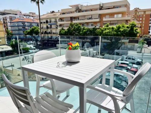 Moderna terraza en la azotea de Fuengirola con mesa de comedor, flores y vistas a la ciudad sobre aparcamiento