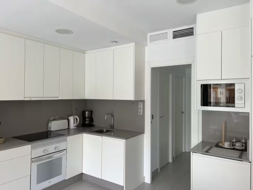 Cocina moderna blanca en apartamento de lujo en Fuengirola con encimeras grises, electrodomésticos de acero inoxidable e integrados