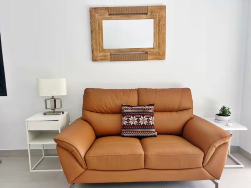 Elegante sala de estar en Fuengirola con sofá de cuero tostado, espejo de madera y mobiliario moderno