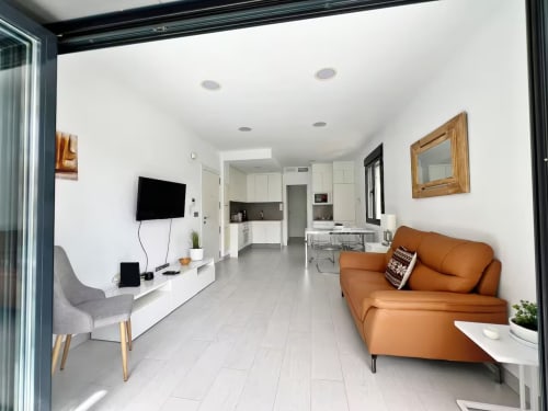 Apartamento de lujo moderno en Fuengirola con sala abierta, sofá naranja, TV, cocina y mobiliario contemporáneo