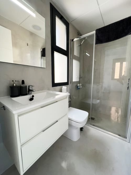 Baño moderno en apartamento de lujo de Fuengirola con tocador blanco, ducha de cristal, inodoro y espejo