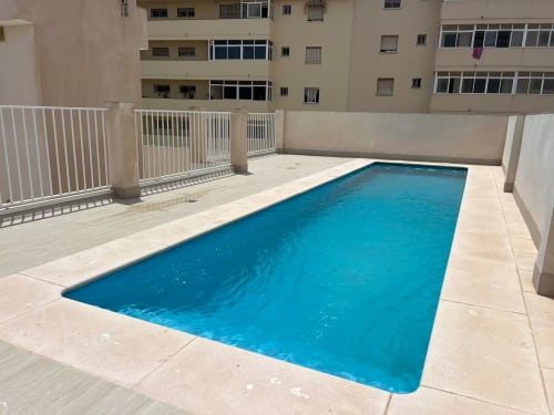 Lujosa piscina de apartamentos en Fuengirola con agua azul, terraza blanca y edificios residenciales circundantes