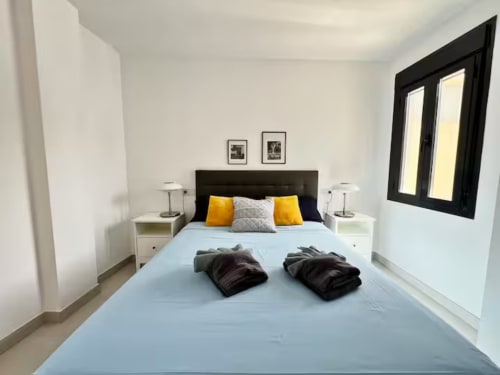 Dormitorio de apartamento de lujo moderno en Fuengirola con cabecero negro, ropa de cama azul claro, detalles amarillos y marcos negros