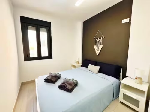 Dormitorio de lujo moderno en apartamento de Fuengirola con cama queen, pared de acento oscura, decoración macramé y muebles contemporáneos