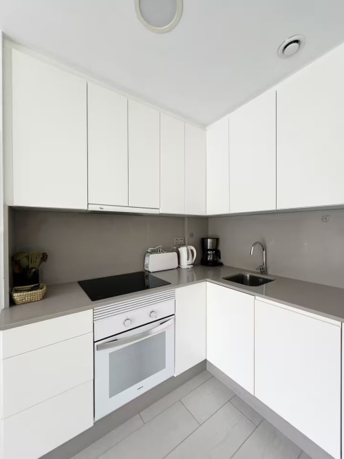Cocina moderna blanca con encimeras grises, electrodomésticos de acero inoxidable y almacenamiento integrado en lujoso apartamento de Fuengirola