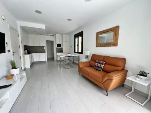 Moderno apartamento de lujo en Fuengirola con salón abierto, sofá naranja, cocina blanca y acceso a piscina