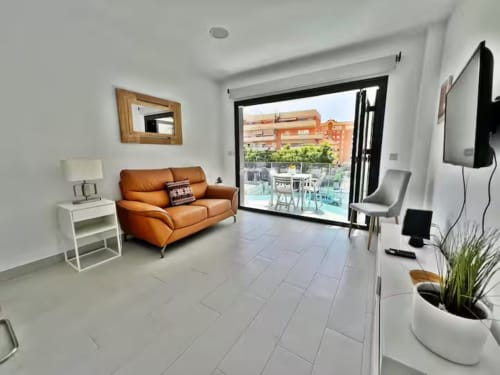 Lujoso apartamento moderno en Fuengirola con sofá naranja, terraza con vista a la piscina y baldosas blancas