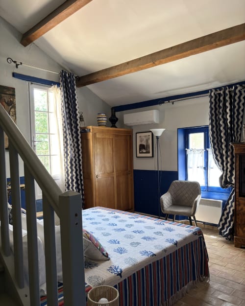 Chambre Suite Fleur au Domaine Du Commandeur avec mur d'accent bleu, poutres en bois, rideaux à motifs et vue sur le jardin