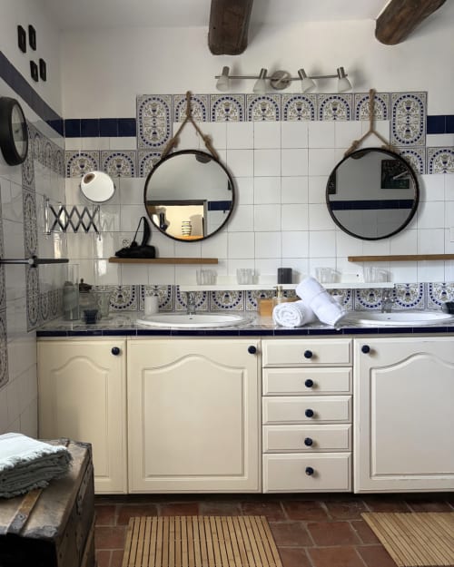 Salle de bains élégante au Domaine Du Commandeur avec carreaux marocains bleu et blanc, miroirs ronds jumelés, vasque crème et rustique