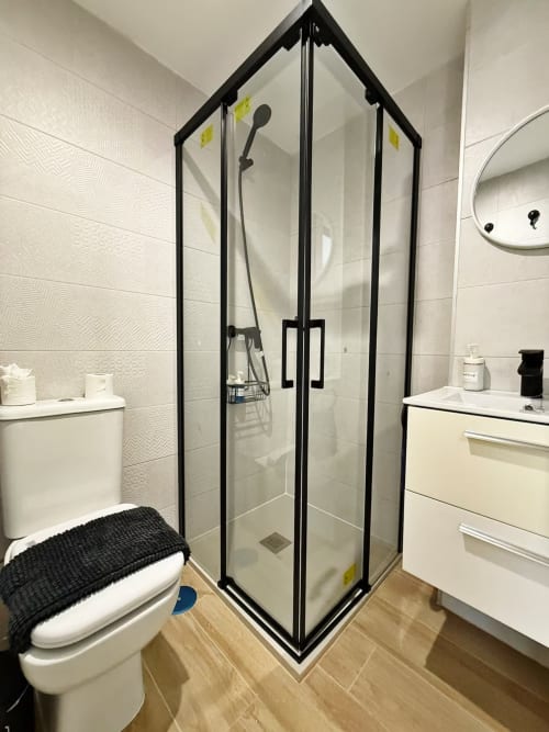 Baño moderno con cabina de ducha de marco negro, tocador blanco y pisos de cerámica en apartamento de playa en Fuengirola