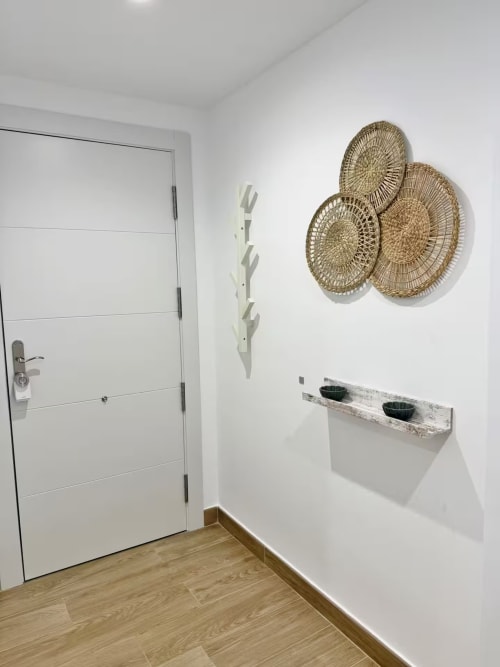 Entrada moderna de apartamento de playa en Fuengirola con puerta blanca, cestas tejidas en la pared y piso de madera