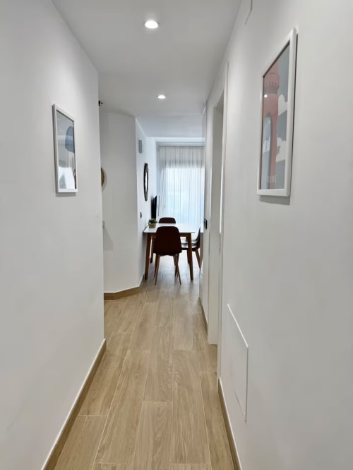 Pasillo moderno en apartamento frente al mar en Fuengirola con suelos de madera, paredes blancas y arte contemporáneo