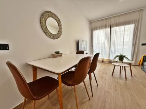Área de comedor de apartamento moderno frente al mar en Fuengirola con mesa blanca, sillas marrones y balcón con vistas al océano