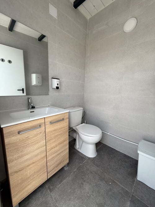 Baño moderno en apartamento de playa de Fuengirola con tocador de madera, inodoro blanco y azulejos grises