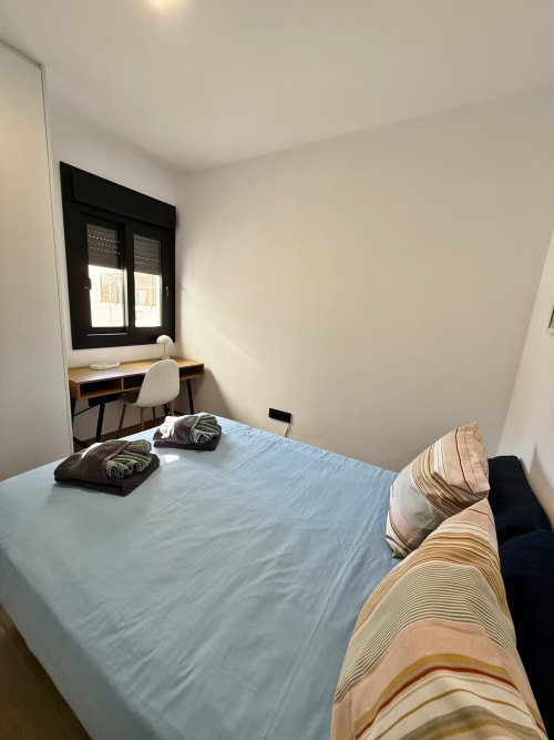 Moderno dormitorio de apartamento en playa en Fuengirola con cama, escritorio, ventanal negro y decoración minimalista