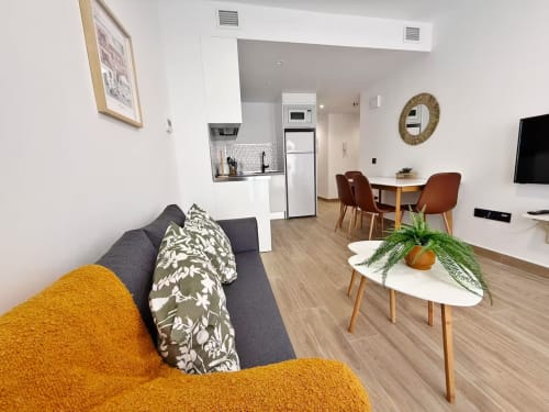 Apartamento moderno en la playa de Fuengirola con sofá gris, sillón amarillo, comedor y cocina abierta