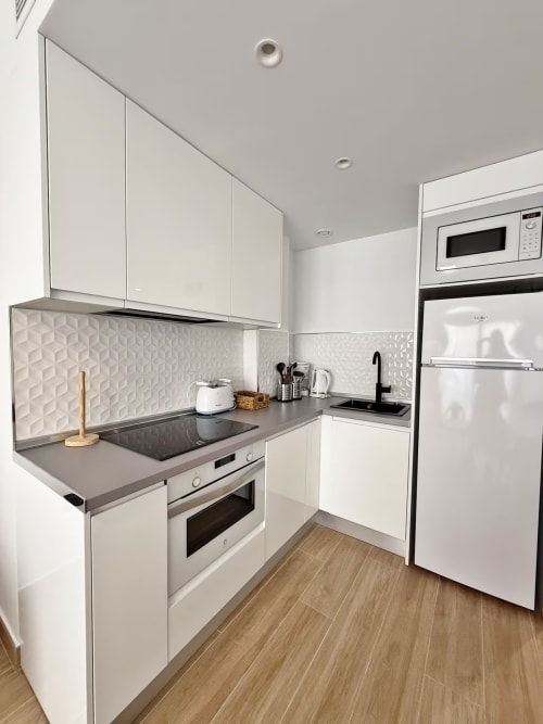 Cocina moderna blanca con encimeras negras, backsplash texturizado y electrodomésticos de acero inoxidable en apartamento frente al mar