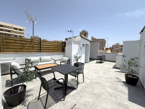 Moderna terraza en la azotea del apartamento de Fuengirola con mobiliario de comedor, zona de descanso, plantas en macetas y vistas a la ciudad