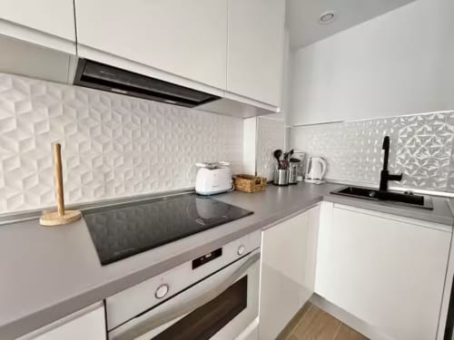 Cocina moderna blanca en apartamento frente al mar en Fuengirola, con encimera, estufa y salpicadero texturizado en negro