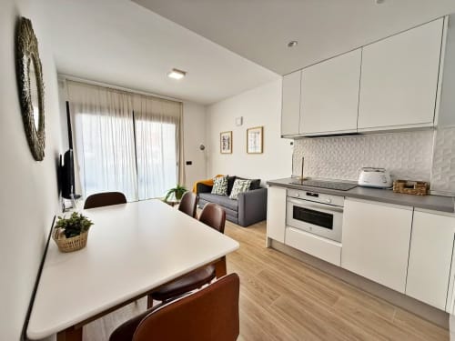 Cocina y comedor modernos en apartamento frente al mar, Fuengirola. Mobiliario blanco, mesa de comedor y sala de estar.