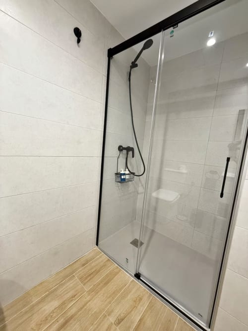 Moderno baño con ducha de vidrio y marco negro, alcachofa de lluvia y manija móvil en apartamento de playa