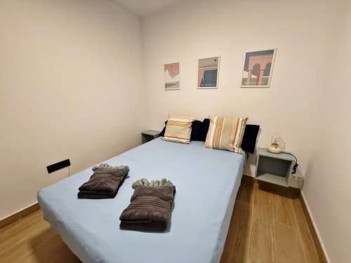 Dormitorio moderno en apartamento de playa en Fuengirola con cama azul, almohadas a rayas y pósters de decoración costera