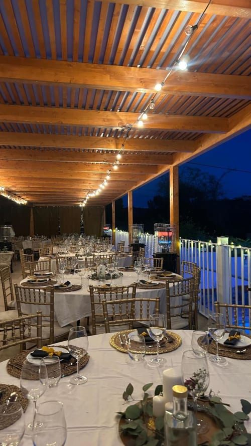 Elegante ambiente de jantar ao ar livre na Quinta dos Lobos com pérgula de madeira, luzes decorativas, mesas redondas e céu azul ao entardecer