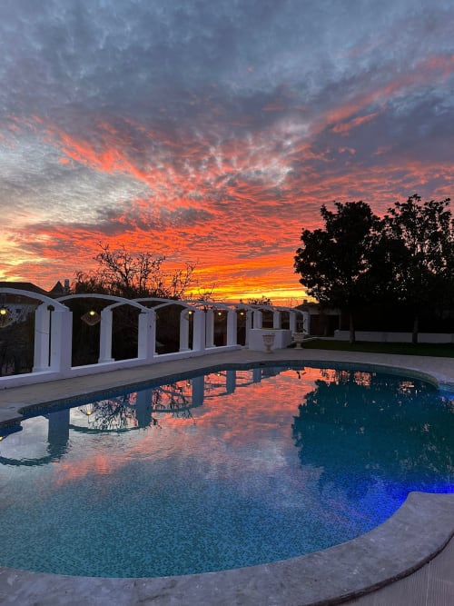 Reflexo do pôr do sol na piscina curva do Quinta dos Lobos Boutique Hotel, Sintra, com edifícios brancos