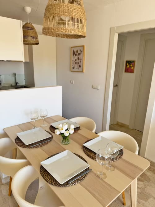 Zona de comedor en apartamento frente al mar en Fuengirola con mesa de madera, lámparas colgantes de mimbre y vistas a la ciudad